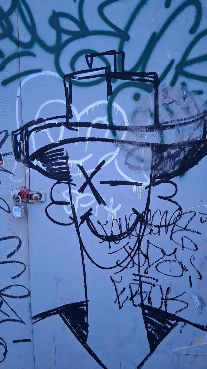 Blue street-art mural of a face wearing a wide-brim hat painted across a wall and door